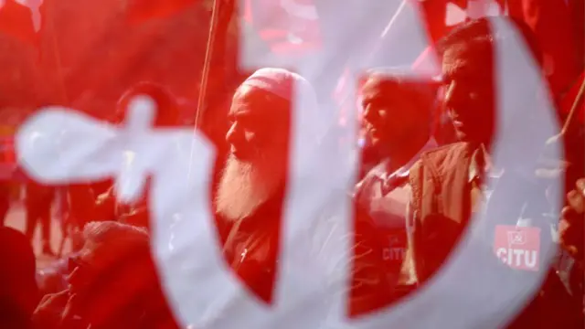 Miembros del sindicato indio vistos a través de una bandera comunista durante una protesta en Nueva Delhi.