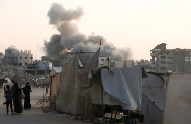 Palestinians stand as smoke rises following an Israeli strike, in Gaza City, August 20, 2025. REUTERS/Dawoud Abu Alkas