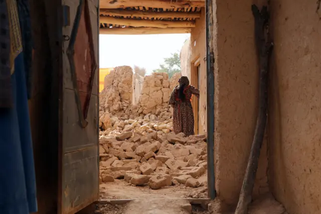 زنی در میان ویرانه‌های خانه خود ایستاده است