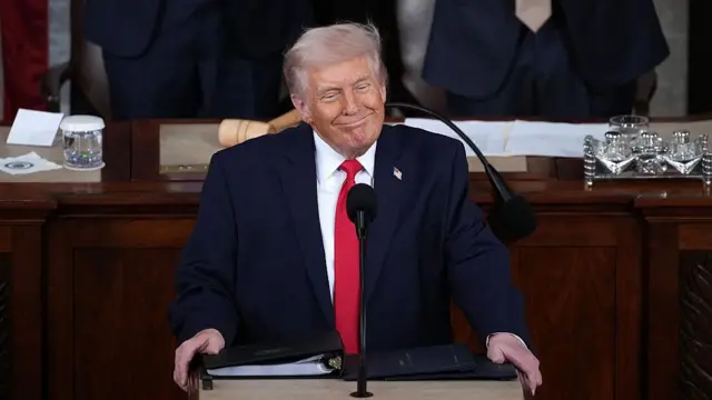 Donald Trump kürsüde, keyifli bir şekilde gülüyor.