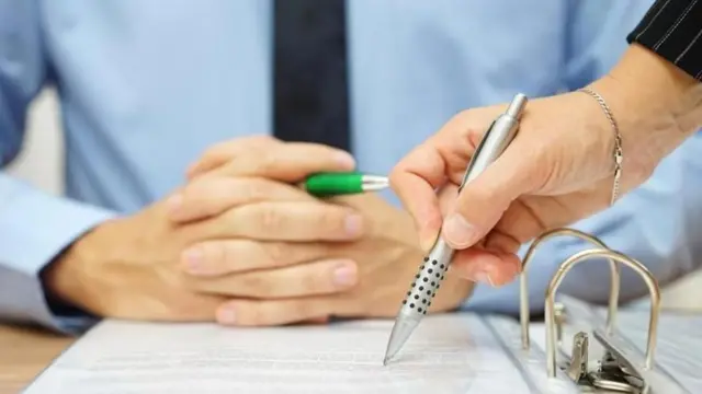 سيدة تكتب في ورقة أمام رجل جالس على مكتب