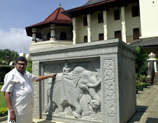 Former chief lay custodian of Sri lanka's holiest Buddhist shrine, Neranjan Wijeyeratne, points to a monument 16 January 2001 set up to commemorate the restoration of the Temple of the Tooth (in the background) after a suicide bomb attack on 25 January 1998. 