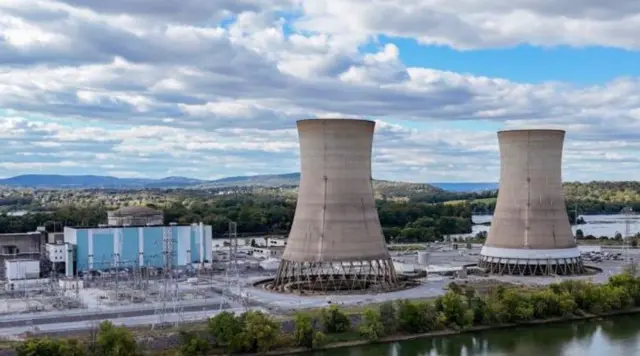 برجا تبريد ضخمان في جزيرة ثري مايل، على يسارهما محطة الطاقة ذات الألوان الزرقاء والبيضاء. السماء من فوقهما زرقاء ومليئة بسحب بيضاء، وبجانبهما مياه.