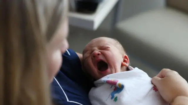 Seorang bayi laki-laki yang baru lahir menguap saat duduk dipangkuan ibunya di AS.