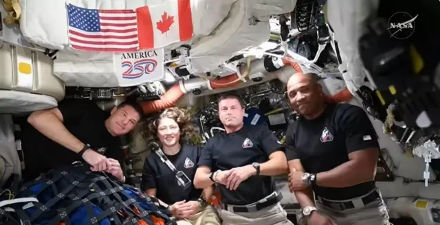 アメリカとカナダの国旗が並び、その下に「アメリカ250年」と書かれた幕も下がる下、オリオンの船内で黒いTシャツを着た4人が並んでカメラに向かっている。シャツの胸についたワッペンは、月から地球へ帰還するイメージを描いたものに変わっている