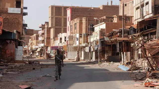 أحد أفراد القوات المسلحة السودانية يتجول بين المباني المتضررة، بعد مرور ما يقرب من عام على الحرب بين القوات المسلحة السودانية وقوات الدعم السريع شبه العسكرية، في أم درمان