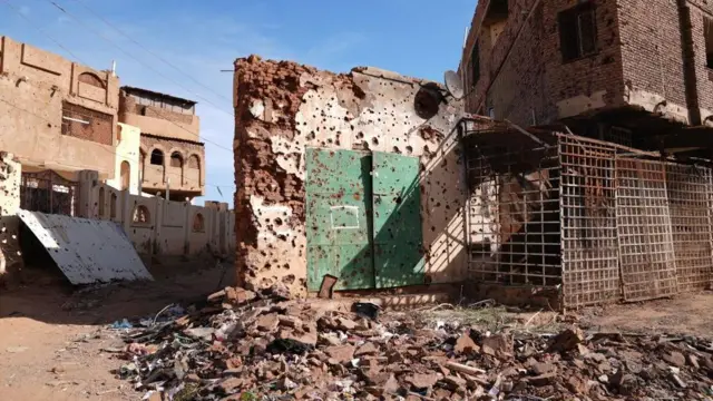 A pockmarked and destroyed building in Khartoum, with rubble in the foreground.