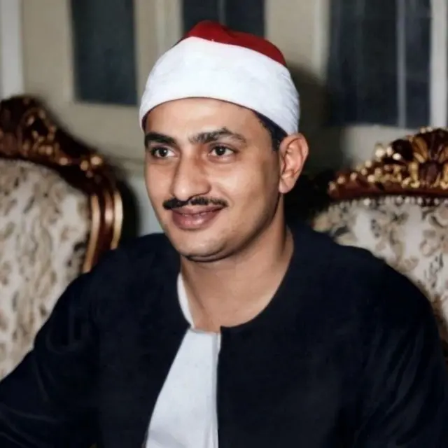صورة الشيخ محمد صديق المنشاوي مبتسماً وهو يرتدي العمة البيضاء بالطربوش الأحمر وجلباباً أبيض والقفطان