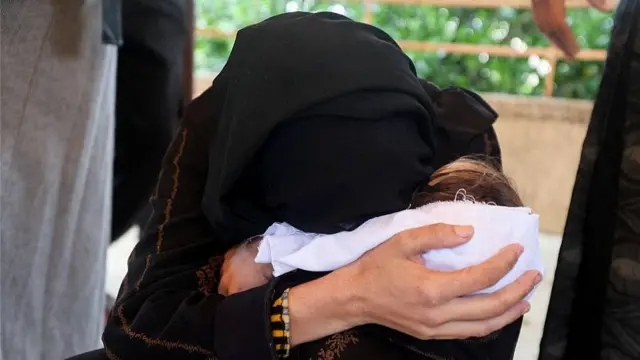 La madre de la bebé Rahaf Abu Jazar abraza a su hija que está envuelta en una sábana blanca.