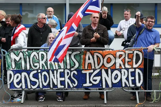 Personas con letreros que dicen "Migrantes adorados, pensionados ignorados". 