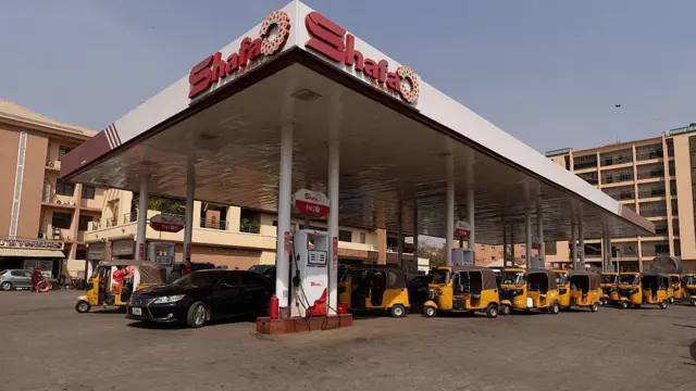 Yellow tuk tuks queueing on the concourse of a petrol station.