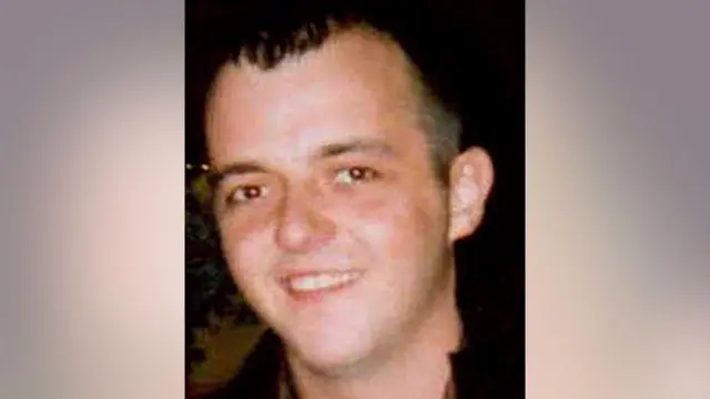 Head shot of Michael Lyons, who is wearing a jacket with a black collar. He is smiling and looking at the camera. He has short black hair, combed forward.
