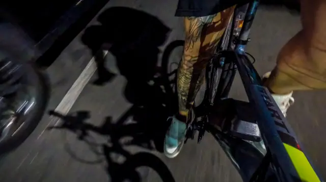Close em uma perna pedalando uma bicileta ao lado de um carro