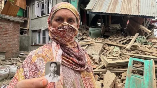 कश्मरीको पहलगाम आक्रमणमा संलग्न भएको आशङ्का गरिएका आदिल ठोकरकी आमा उनको तस्बिर बोकेर सुरक्षाकर्मीहरूले भत्काइदिएको आफ्नो घरअगाडि