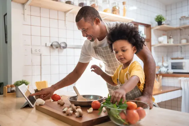 Pai preparando refeição com a filha na cozinha de casa