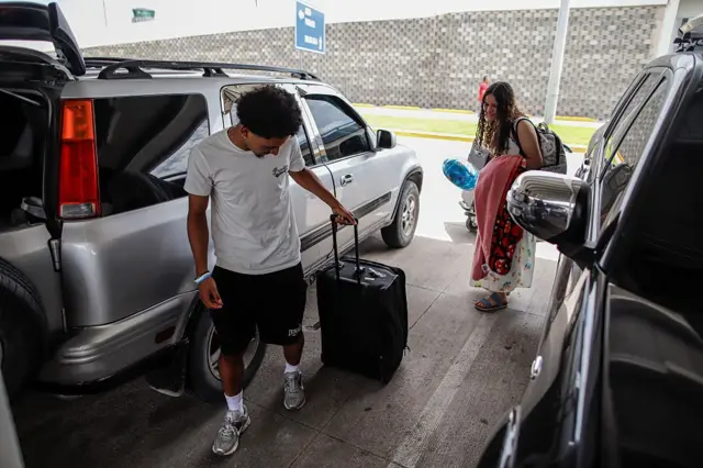 Emerson Colindres arrastra una maleta entre dos coches en un parking, seguido de cerca de su hermana, Alison Colindres, en el aeropuerto de Tegucigalpa el 24 de junio de 2024. (Foto: JORGE CABRERA/AFP via Getty Images)