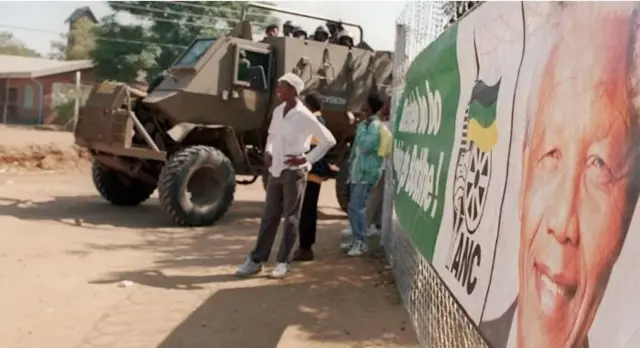 Ndị mmadụ kwụ n'akụkụ ụgbọala ndị agha