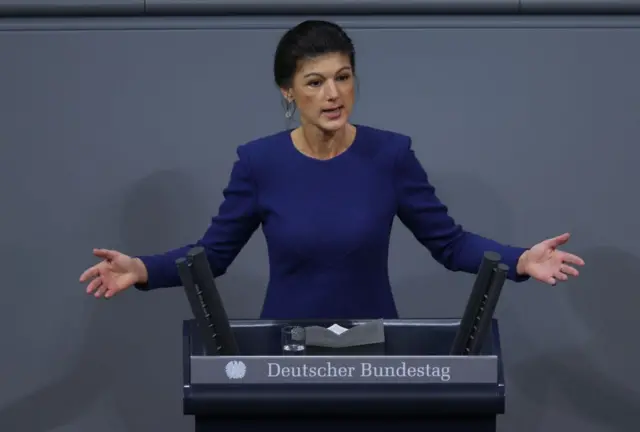 Sahra Wagenknecht lacivert bir elbise giymiş, mecliste konuşuyor.