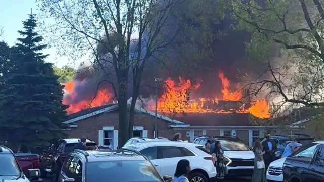 Abantu bateraniye ahantu, mu gihe umwotsi uzamuka hamwe n'umuriro, nyuma y'ibyabaye, aho umugabo yinjije imodoka ye mu muryango w'urusengero i Michigan akarashisha imbunda ndetse agatwika urusengero, mu mujyi wa Grand Blanc, muri leta ya Michigan, muri Amerika, ku itariki ya 28 Nzeri (9) mu mwaka wa 2025.