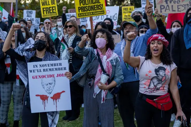 امرأة تحمل لافتة مكتوب عليها "في نوفمبر سوف نتذكر" و"جو الداعم لللإبادة" مع وجه بايدن ويدين عليهما دماء