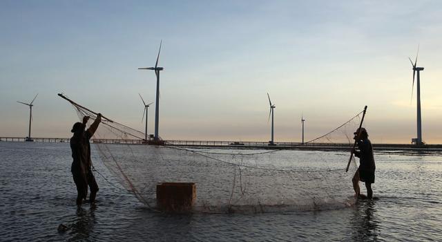 Bức ảnh này chụp ngày 2/5/2014, cho thấy ngư dân đang làm việc gần những tua-bin gió của nhà máy điện gió đầu tiên của Việt Nam dọc theo bờ biển Bạc Liêu