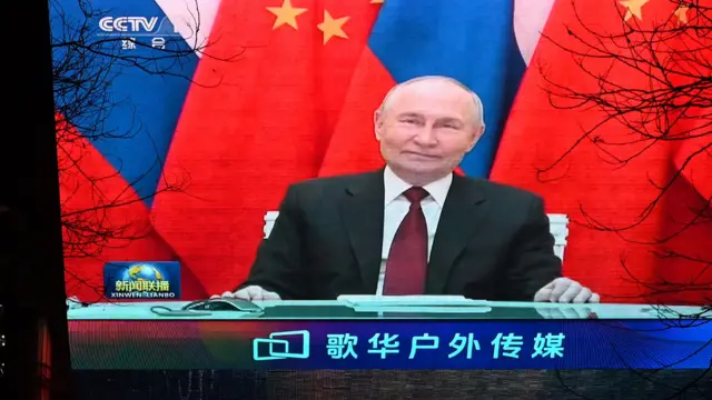 Улыбчивый Путин на фоне китайского и российского флагов на телеэкране в китайском торговом центре