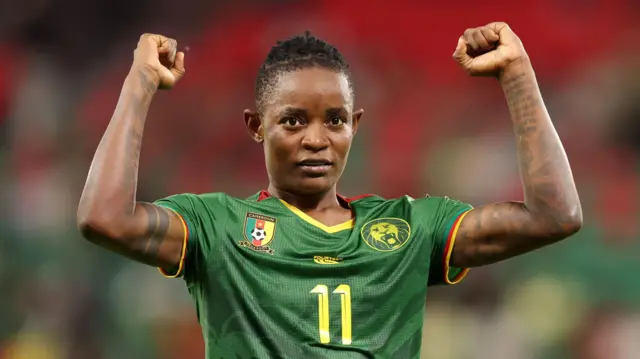 Marie Ngah Manga, vêtue d'un maillot vert du Cameroun floqué du numéro 11 jaune, lève les bras, poings serrés, en signe de victoire.