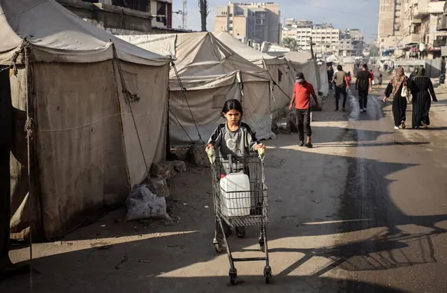فتاة فلسطينية نازحة تحمل وعاء ماء إلى خيمتها أمام مدرسة الفارابي، التي تحولت إلى مأوى بعد أن تعرضت لضربة إسرائيلية، في مدينة غزة، بتاريخ 7 سبتمبر/أيلول 2025.