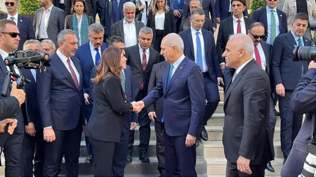 Kurtulmuş bir merdivenin basamaklarının dibinde bir kadınla tokalaşıyor.