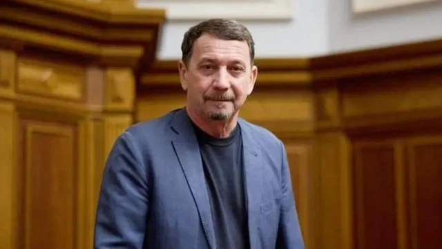 Мужчина средних лет с бородой в пиджаке поверх черной футболки.