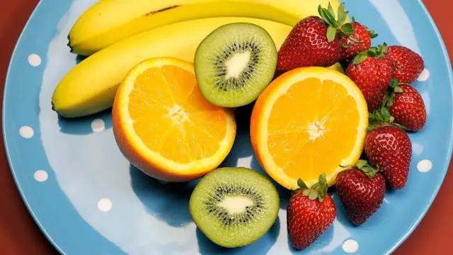 Prato azul com frutas, com banana, laranja, kiwi e morangos