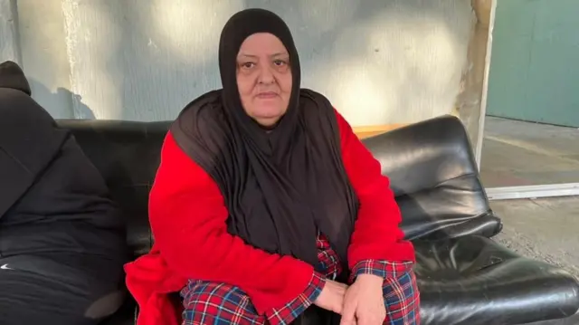 امرأة لبنانية ترتدي سترة حمراء تجلس على أريكة سوداء.
