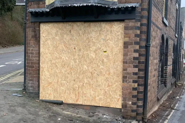 Un edificio victoriano de ladrillo en la intersección en forma de V de dos calles, con un gran cuadrado de madera en la fachada. El edificio tiene arcos de ventanas y otros detalles en ladrillo negro.
