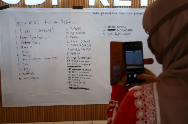 Seorang perempuan sedang memotret papan pengumuman data korban selamat KMP Tunu Pratama Jaya.