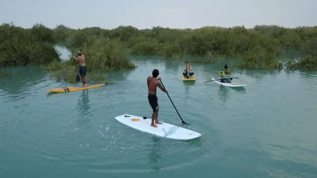 جزیره قشم، ایران – ۱۰ اسفند ۱۳۹۹: گروهی از جوانان روی تخته‌های پارویی در آب‌های آرام جنگل‌های مانگرو حرا استراحت کرده و خوش می‌گذرانند. زنان لباس‌های ویژه‌ای بر تن دارند تا موازین پوشش اسلامی را رعایت کنند. ایرانی‌ها به جزایر خلیج فارس سفر می‌کنند تا به دلیل محدودیت‌های کمتر اعمال‌شده توسط دولت، اوقات فراغت خود را سپری کنند.
