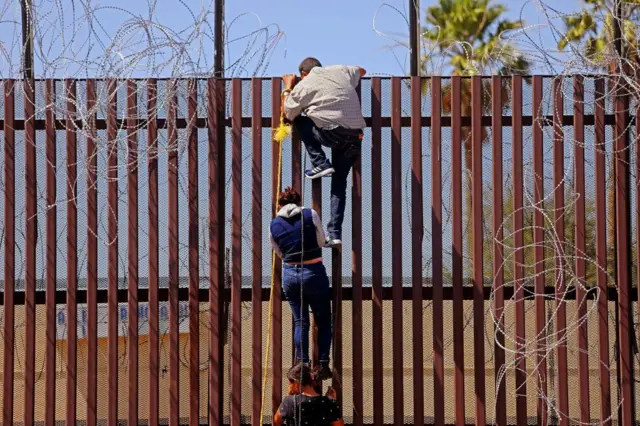 Migrantes intentan trepar la barrera fronteriza desde Mexicali, México hacia Calexico, EE. UU., el 13 de mayo de 2023 en Mexicali, Baja California. +Gary Coronado / Los Angeles Times vía Getty Images)