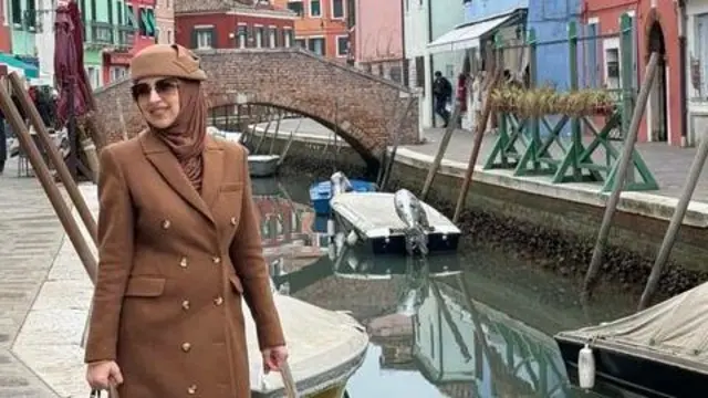 Žena u braon kaputu sa braon maramom i šeširom na glavi