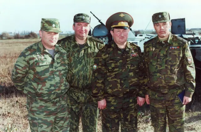 Генералы Трошев и Герасимов в камуфляже стоят на фоне военной техники вместе с двумя другими военными
