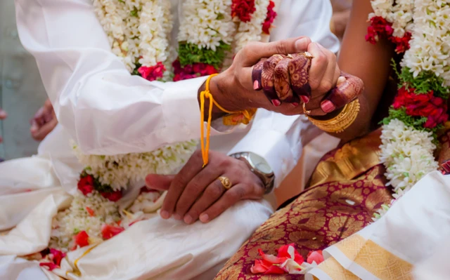 Deux mariés assis côte à côte, se tenant la main, lors d'un rituel de mariage en Inde.