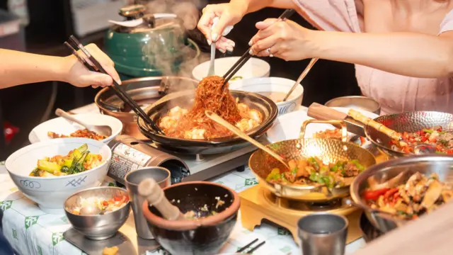 Several dishes placed on a table at a branch of Nong Geng Ji, a popular Hunan restaurant chain in Singapore. Two customers (faces not in frame) are tucking into a spicy noodle dish at the centre of the table