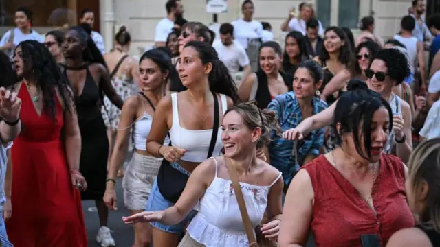 Grupa ludzi, głównie kobiet, tańczy na ulicy podczas francuskiego festiwalu Fête de la Musique