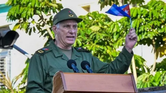 Diaz-Canel, presidente de Cuba, falando em um púlpito e segurando a bandeira de Cuba