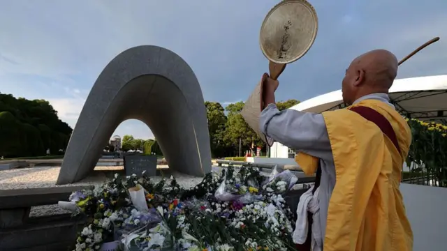 አንድ መነኩሴ አበቦች የተቀመጡበት መታሰቢያ ፊት ለፊት ቆመው