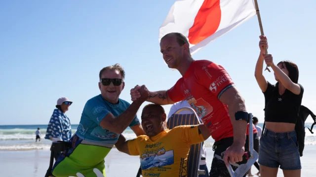 Em clima de comemoração, Llywelyn Williams e outros dois surfistas posam para uma foto após a competição, com o mar ao fundo