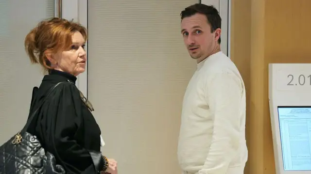 Пьер Бурден в белом свитере вполуоборота, рядом с какой-то женщиной.