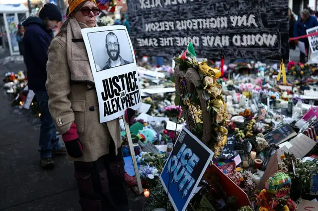 Uma mulher segura uma placa com os dizeres "Justiça para Alex Pretti" no memorial improvisado montado perto da rua onde ele foi baleado e morto por agentes federais de imigração em Minneapolis, Minnesota