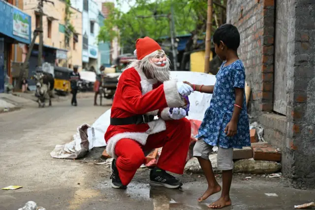 A man dressed in Santa Claus outfit shakes hand and offers chocolates to a child ahead of Christmas in Chennai, on December 24, 2024.