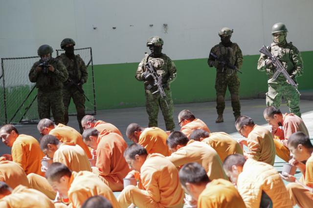 Prisioneros en Ecuador miran al suelo sentados y con trajes naranja delante de efectivos de seguridad fuertemente armados
