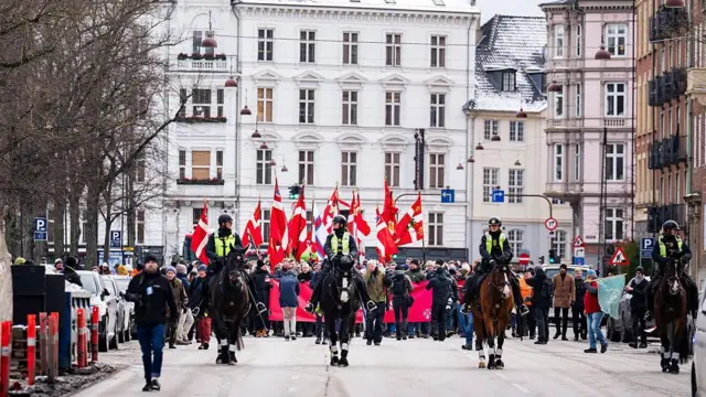 Grönland'da atlı polisler ve arkalarında eylem yapan bir kitle görülüyor.