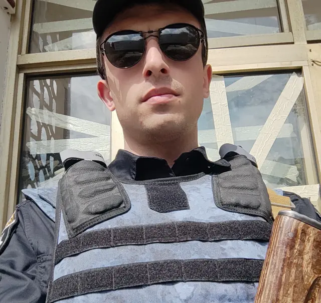 Молодий чоловік у бронежилеті зі зброєю у темних окулярах 